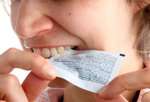 A woman biting a medicine packet open.
