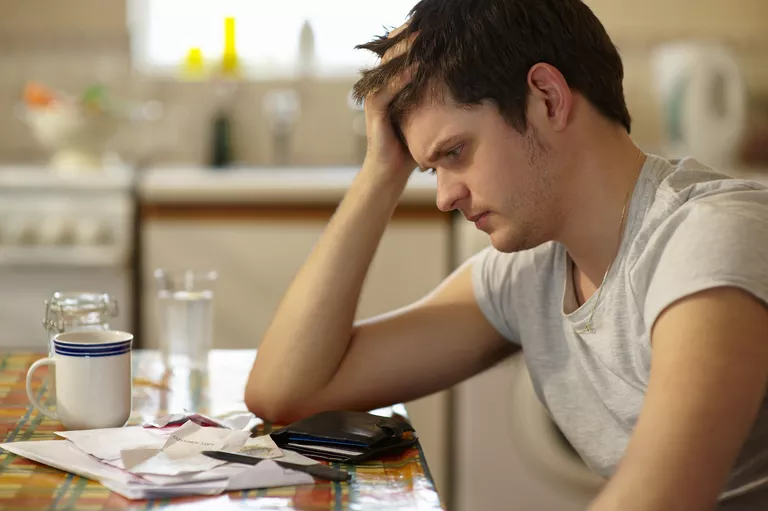 Young man holding head looking at receipts.
