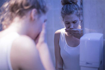 Photo of a nauseated young woman standing in a bathroom.